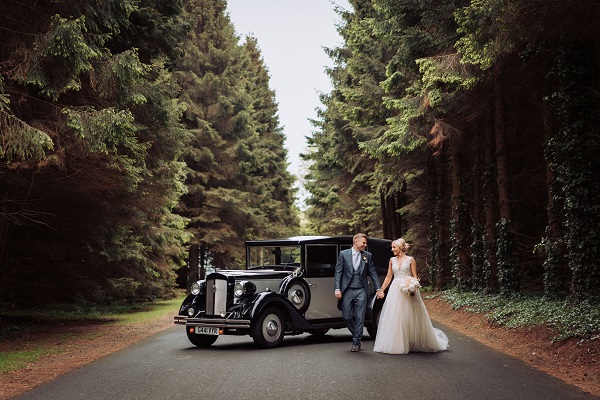 Wedding couple standing in front of wedding car in the woodland surroundings of Montalto Estate
